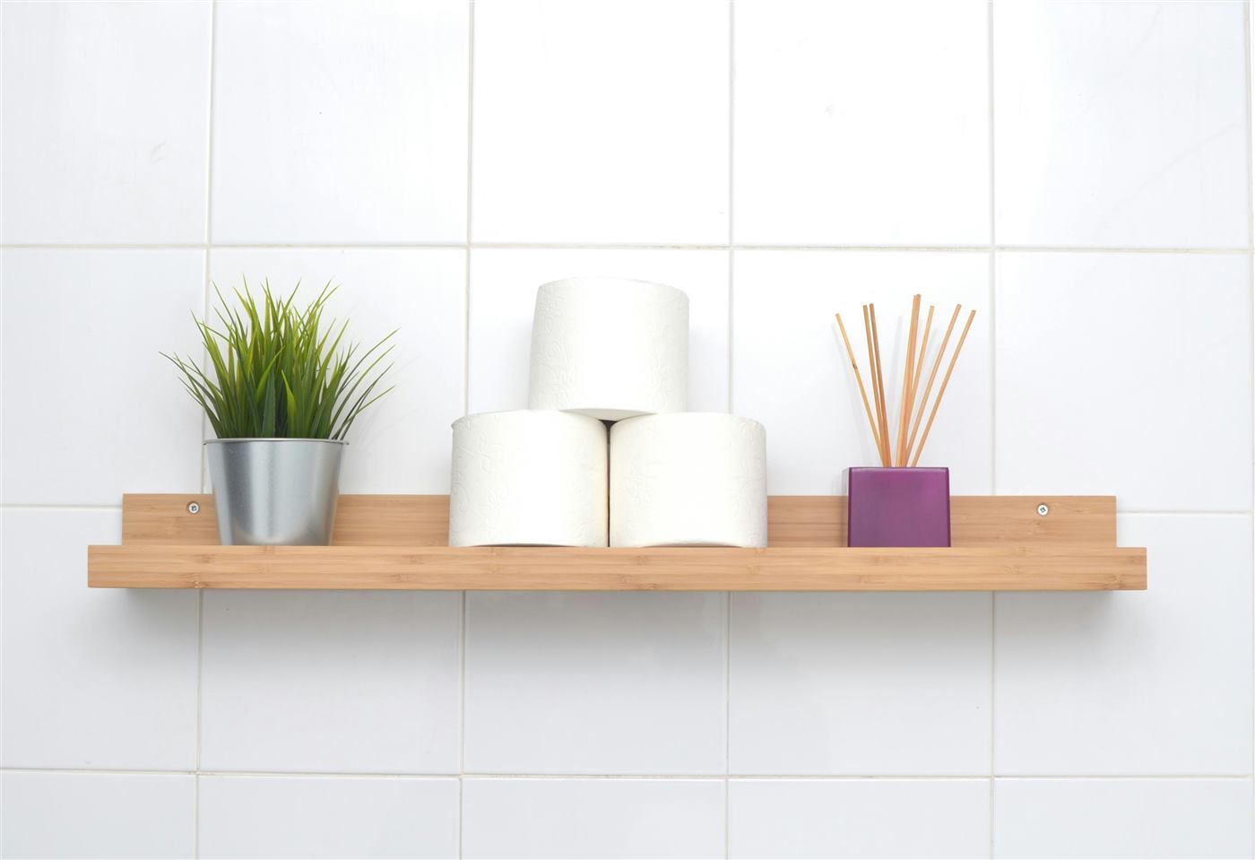 Wooden wall shelf on white tiles holding a plant, toilet paper rolls and a reed diffuser