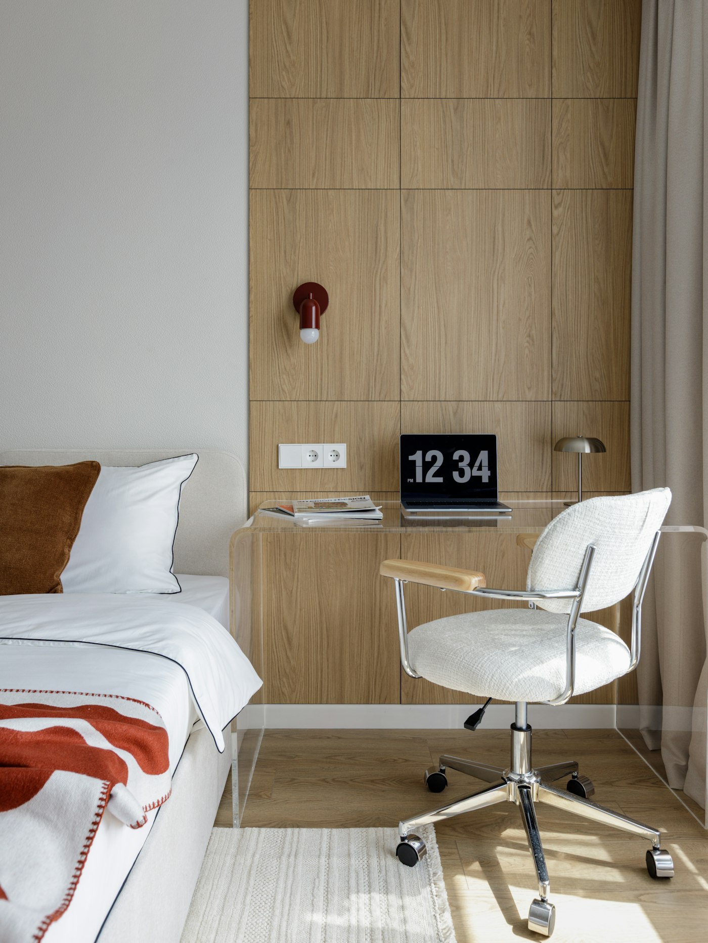 Small desk with a laptop and a white office chair beside a bed in a bright bedroom